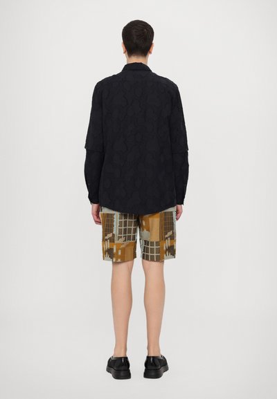 Schwarzes Langarmshirt mit strukturiertem Muster, kombiniert mit gemusterten Shorts in Erdtönen, die geometrische Designs und einen geraden Schnitt aufweisen.