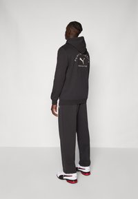Mørkegrå hættetrøje med et logo på ryggen, parret med matchende sweatpants. Materialet virker blødt; har en afslappet pasform og minimalistisk design.