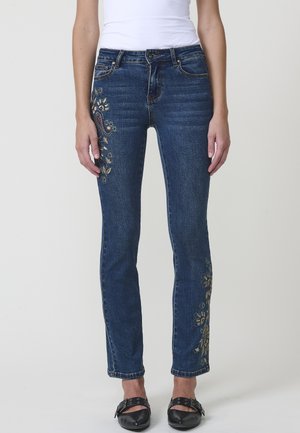 Jeans de mezclilla azul con un corte ajustado, que presentan bordados florales en la parte delantera y un cierre tradicional de botón y cremallera.