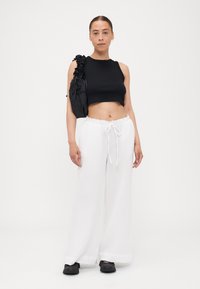 Black cropped sleeveless top, white wide-leg pants with drawstring waist, and chunky black shoes. Textured fabric and ruffled bag detail.