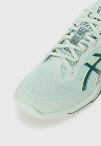 Light blue athletic shoe with mesh upper, textured patterns, and green accents. Features laces and a smooth rubber sole.