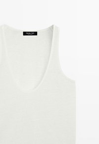Débardeur blanc sans manches à encolure dégagée avec une étiquette noire portant la mention « Massimo Dutti » au niveau du col.