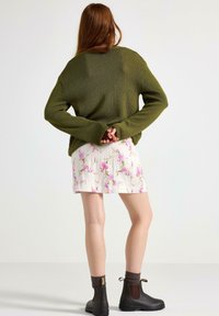 Grøn strikket sweater, hvid plisseret nederdel med pink blomsterprint, brune ankelstøvler med elastiske sider og brune ribbede sokker.