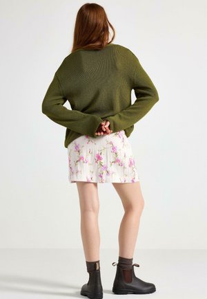 Nadměrný olivově zelený pletený svetr, květinová plisovaná sukně s růžovými květy, kotníkové hnědé boty a hnědé žebrované ponožky.