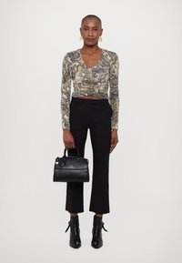 Langsleeve, aansluitend bovenstuk met een slangenprint in beige en zwart; gecombineerd met zwarte, hoge taille broek en enkellaarsjes. Handtas is van zwart leer.