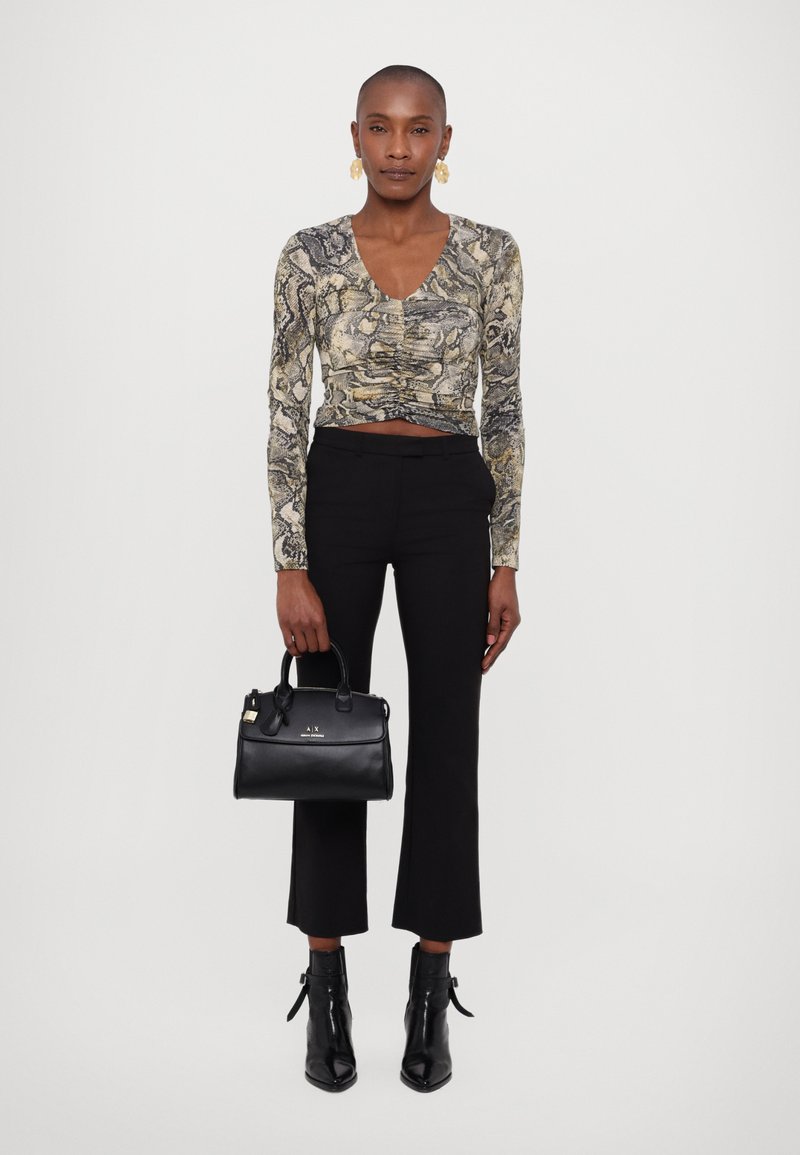 Langsleeve, aansluitend bovenstuk met een slangenprint in beige en zwart; gecombineerd met zwarte, hoge taille broek en enkellaarsjes. Handtas is van zwart leer.