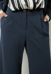 Marineblauwe wijde broeken van soepele stof met zijzakken en een subtiele klepsluiting aan de taille.