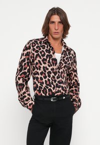Leopard-print long-sleeve shirt in hues of pink and black with a collared neckline; paired with black trousers and a black belt.