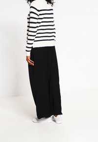 Maglione a righe in bianco e blu marine, abbinato a una maxi gonna nera. Presenta una vestibilità ampia e sneackers bianche per un look casual.