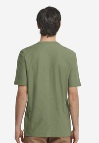 Olivgrön t-shirt med kort ärm i mjukt tyg, med rund hals och avslappnad passform som har en subtil textur.