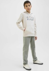 Bēšas kapucētas sporta krekls ar "JACK & JONES" grafiku, ar priekšējo kabatu; apvienots ar gaiši zaļu biksēm un bēša/pelēku kedām.