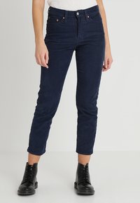 Pantalon en velours côtelé bleu marine avec une coupe slim, taille haute et longueur raccourcie, doté de poches avant et d'une braguette à boutons.