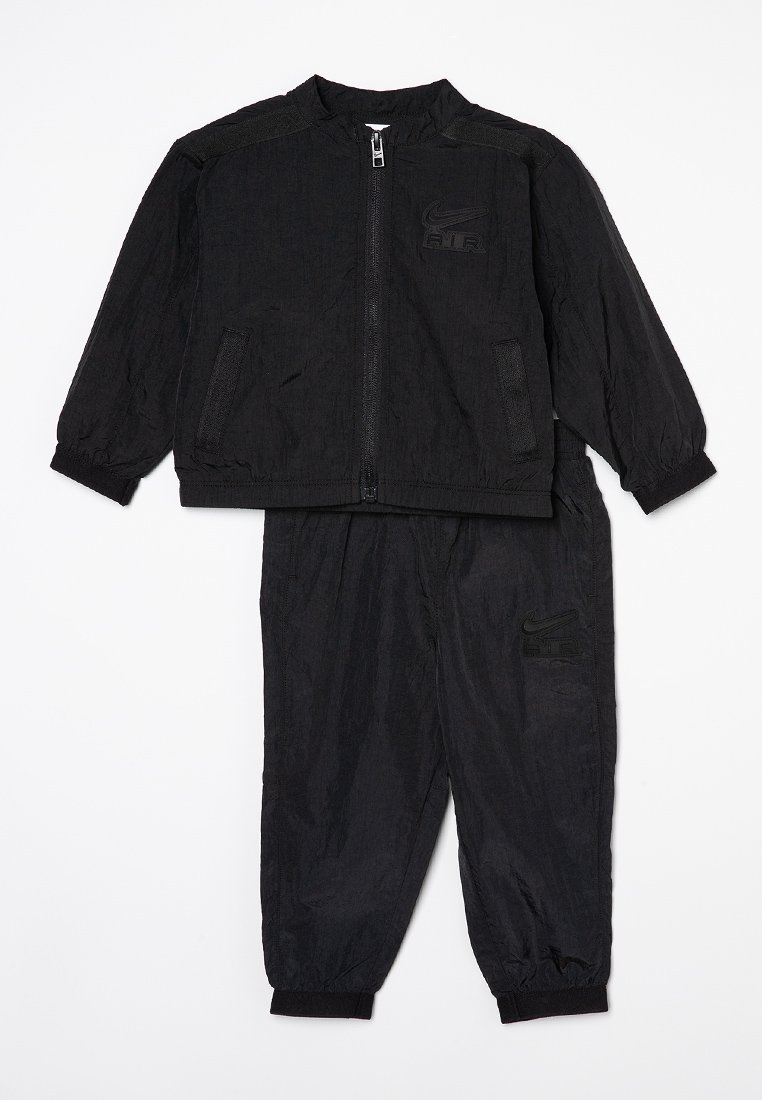 Ensemble de jogging noir Nike avec une veste zippée et un pantalon. Comprend des poignets élastiques et des poches. La veste a un détail de logo en relief. Matière légère.