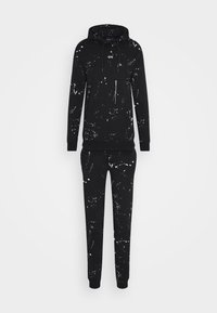 Ensemble sweat à capuche et pantalon de survêtement noirs avec motif éclaboussures de peinture blanche, poche kangourou à l'avant et capuche avec cordon de serrage.