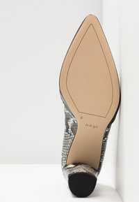 Chaussure à talon aiguille avec un design imprimé serpent noir et blanc, bout pointu, doublure noire lisse et une semelle beige avec détail de logo.