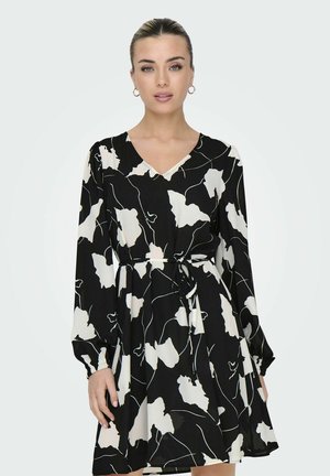 Robe noire avec un motif floral abstrait blanc, décolleté en V, manches longues, taille ceinturée et jupe fluide. Tissu lisse avec un léger éclat.