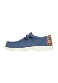 Scarpa slip-on in denim blu con suola bianca maculata. Presenta dettagli pattern marroni sul tallone e lacci abbinati.