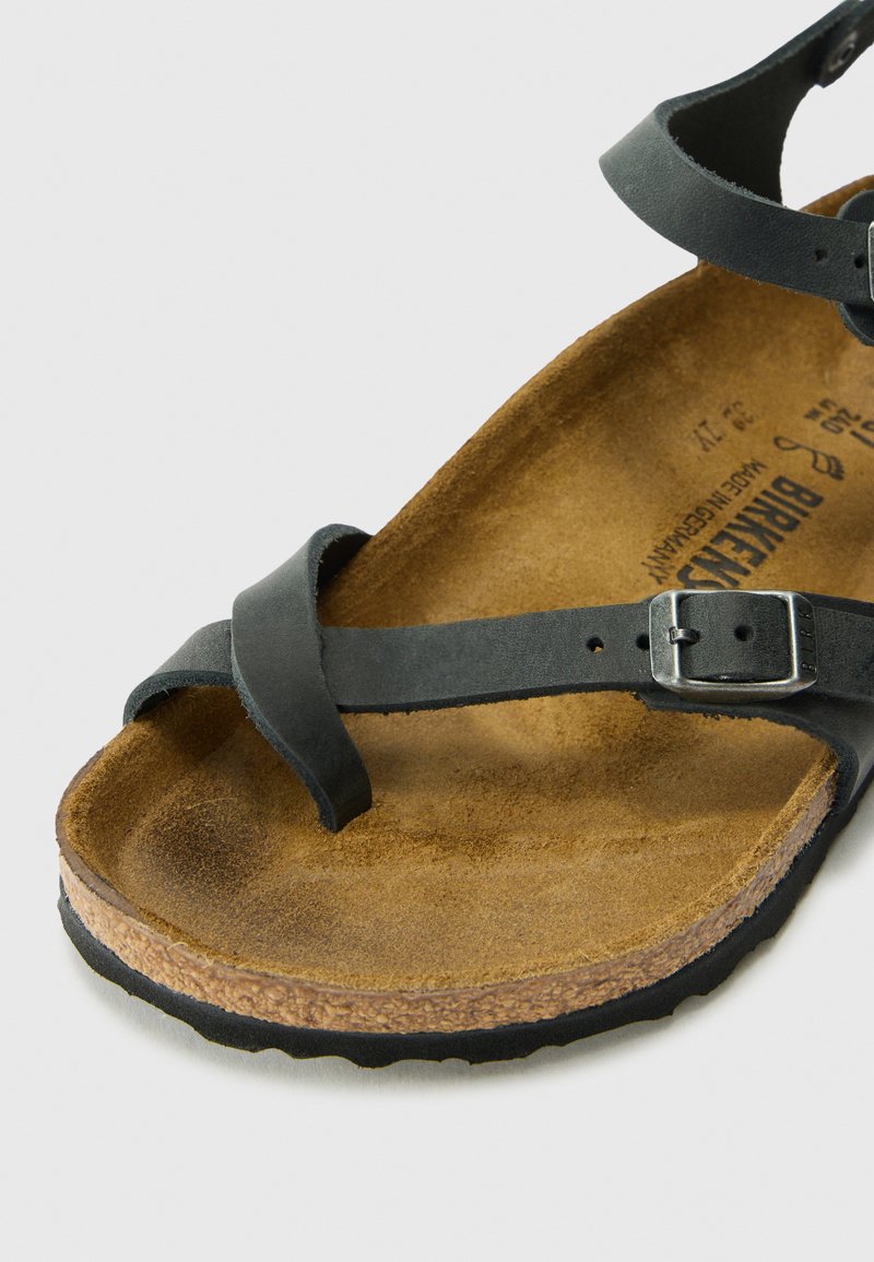 Schwarze Ledersandale mit einem überkreuzten Riemendesign, einer silbernen Schnalle und einem konturierten Fußbett aus braunem Kork. Gummisohle mit strukturiertem Finish.