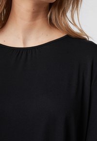Schwarzes Shirt mit rundem Ausschnitt, weichem Material und Raffung am Ausschnitt. Hat eine lässige Passform ohne sichtbare Nähte.