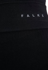 Czarne prążkowane legginsy z szerokim pasem w talii, na którym znajduje się napis „FALKE” w kontrastującym szarym kolorze, prezentujące fakturowany wzór dzianiny.