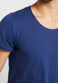 Marinblå t-shirt med kort ärm, rund halsringning, tillverkad av mjuk bomullsblandning, med en slät yta och figurnära passform.