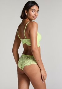 Lime zelena čipkasta bralette in usklajene hlačke z cvetličnimi vzorci, valovitimi robovi in nastavljivimi naramnicami, ki prikazuje polprosojno zasnovo.
