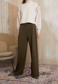 Světle béžový zkrácený svetr s texturovanými balónovými rukávy a dekorativními knoflíky, doplněný olivově zelenými širokými kalhotami. Měkká tkanina, neformální design.