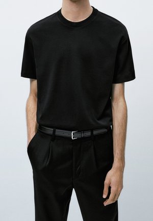 T-shirt en coton noir à manches courtes et col rond, porté avec un pantalon tailleur noir et une ceinture noire avec une boucle en argent.