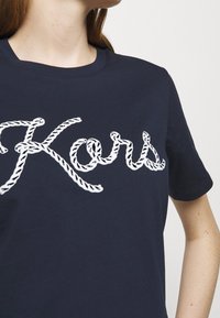Granatowa bawełniana koszulka T-shirt z białym napisem w stylu sznurka, który głosi "Kors", z klasycznym okrągłym dekoltem i krótkimi rękawami.