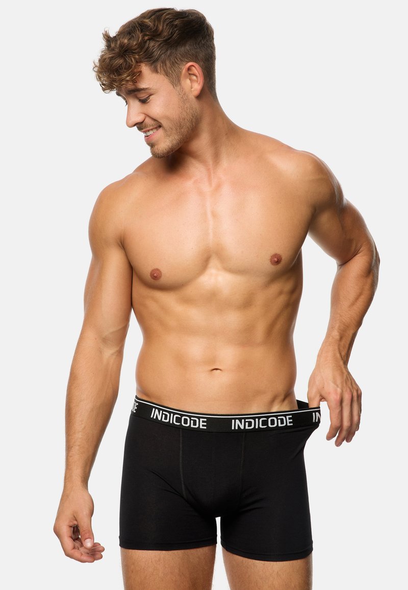 Bóxer negro con una cinturilla de marca que presenta texto blanco. La tela parece suave y ajustada. El modelo está sin camisa, mostrando el diseño.