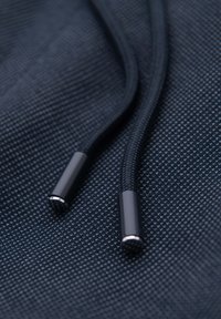 Gros plan d'un tissu bleu foncé avec une texture tissée et des cordons noirs avec des embouts en plastique brillants aux extrémités.