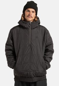 Czarny pikowany pulower z kapturem, z przednim zamkiem błyskawicznym do połowy, sznurkiem do ściągania na kapturze oraz elastycznymi mankietami. Cechuje się charakterystyczną okrągłą fakturą oraz logo na klatce piersiowej.