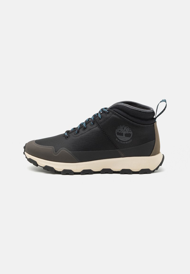 Zapato de senderismo negro impermeable con parte superior de textil, capuchón de goma gris en la punta, cordones azules y suela beige con un patrón de relieve resistente.