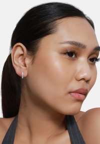 Silberner Creolenohrring am Ohr eines Modells. Der Ohrring verfügt über ein glattes, rundes Design mit polierter Oberfläche, die seine reflektierende Qualität hervorhebt.