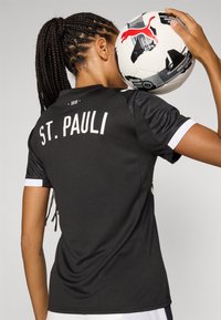Zwarte voetbalshirt met "ST. PAULI" in witte letters op de achterkant, met contrasterende witte accenten op de mouwen en een getailleerd ontwerp.