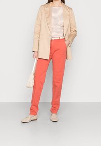 Béžový blazer přes bílý a růžový pruhovaný top, spárovaný s korálovými kalhotami a béžovými mokasíny. Nese malou bílou kabelku.