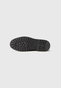 Suela de bota de goma negra con un patrón de profundidad, que presenta formas rectangulares y diamante para ofrecer tracción. Logo de la marca estampado en el área del talón.