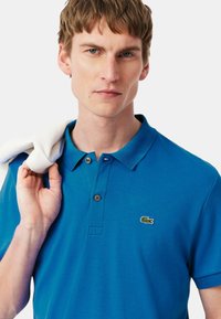 Polo shirt blu con colletto classico, patta con tre bottoni e logo ricamato verde sul lato sinistro del petto. Tessuto di cotone liscio.