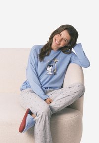 Světle modrý dlouhý rukáv pyžamového trika se Snoopy grafikou a šedé kalhoty s drobnými modrými a červenými květinovými vzory. Měkký, volný střih.