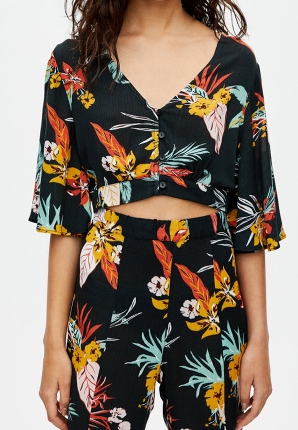 Top corto negro con flores, escote en V, mangas cortas acampanadas y cierre de botones, con coloridos patrones tropicales sobre una tela texturizada.