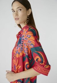 Rode blouse met grote bloempatronen in oranje en groen, korte omgeslagen mouwen met merkdetail, gemaakt van lichtgewicht stof.