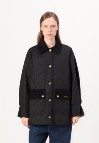 Quilted black jacket, featuring a flat collar, gold hardware, two front pockets, and subtle stitching pattern. Made of textured material.