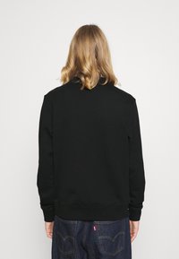 Černá mikina s kulatým výstřihem a pletenými manžetami. Měkká textura, uvolněný střih, bez viditelných vzorů či log, nošená s tmavými džíny.