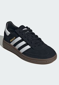 Sapatilha de camurça preta com riscas brancas e logótipo dourado "Spezial". Apresenta atacadores pretos, uma sola de borracha castanha texturizada e um design elegante.