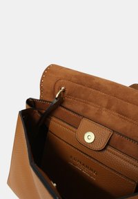 Borsa a tracolla in pelle marrone con patta in suede, hardware dorato, dettagli testurizzati e un interno con tasche strutturate e marchio.