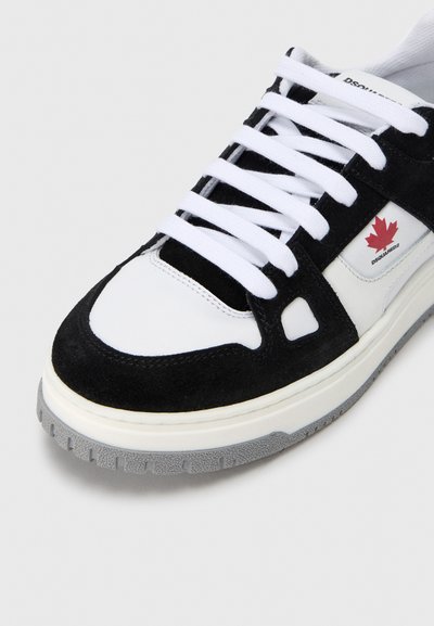 Baskets noir et blanc en daim et cuir, avec des lacets blancs, une semelle épaisse et un logo feuille d'érable rouge sur le côté.