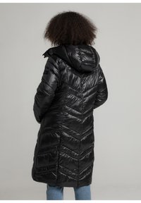 Zwarte pufferjas met capuchon, chevron-stikselontwerp en gewatteerde textuur. Lange lengte met een elegante, gladde afwerking.