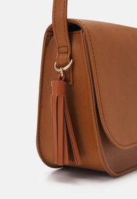 Bolso de cuero marrón con textura suave, forma redondeada y herrajes dorados. Cuenta con un detalle de borla en el lateral.