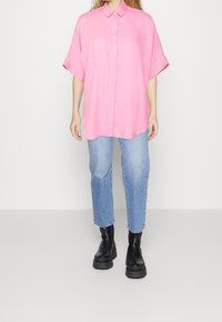 Rosa skjorta med krage och korta ärmar, tillsammans med ljusblå jeans och svarta kraftiga ankelstövlar.