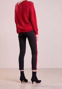 Röd tröja med ribbad struktur, kombinerad med svarta jeans med röda sidostråk. Svarta ankelstövlar med smal klack.